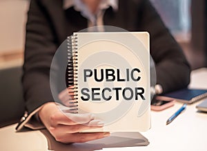 Businesswoman holding a notepad with PUBLIC SECTOR text written on it