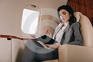 Businesswoman holding pen while looking at notebook in private jet