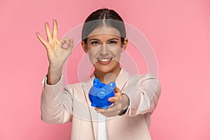 Businesswoman holding a piggy bank and making an ok sign