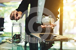 Businesswoman holding a piggy bank while putting coin into a glass jar