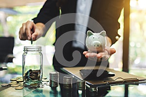 Businesswoman holding a piggy bank while putting coin into a glass jar for saving money concept