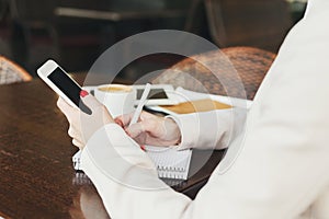 Businesswoman holding smartphone and writing notes closeup outdoors