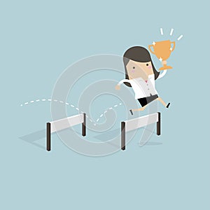 Businesswoman jumping over obstacle and holding trophy.