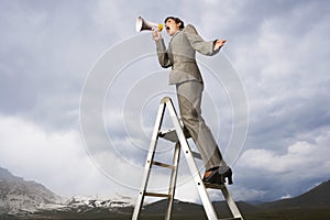 Businesswoman On Ladder Shouting Through Megaphone