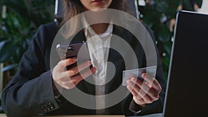 Businesswoman on a laptop makes a purchase via a smartphone, holding credit card. Online shopping