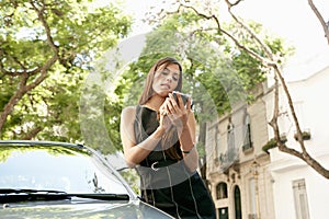 Businesswoman leaning on car with smartphone.