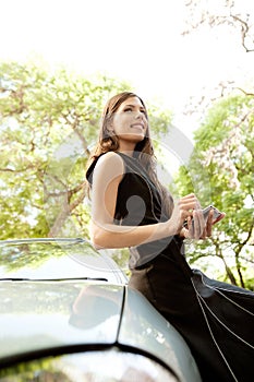 Businesswoman leaning on car with smartphone.