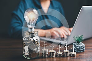 Businesswoman with lightbulb on money jar and using calculator to calculate and money stack. Save energy and money with accounting