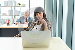 Businesswoman looking at camera behind laptop while doing some paperwork at the office