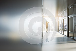 Businesswoman looking out of window in abstract bright light office interior with mock up place on silver wall. Success, future