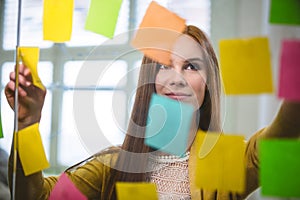 Businesswoman looking at sticky notes on glass