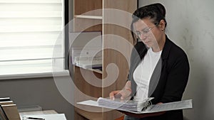A businesswoman looks at a binder of papers. Working with documents in the office