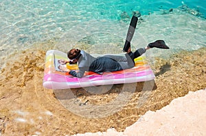 Businesswoman lying on lilo and typing on laptop