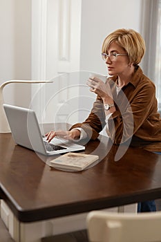Businesswoman. Mature Woman Uses Laptop And Drinks From Cup.