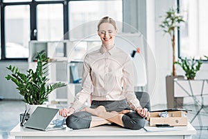 Businesswoman meditating in lotus position on messy table in office