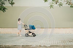 Businesswoman mother and your baby in cart walking on urban sidewalk - stock photo