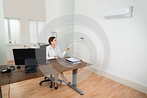 Businesswoman Operating Air Conditioner In Office