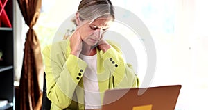 Businesswoman with pain in neck and spine sits in office in front of laptop