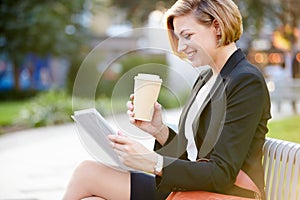 Businesswoman On Park Bench With Coffee Using Digital Tablet