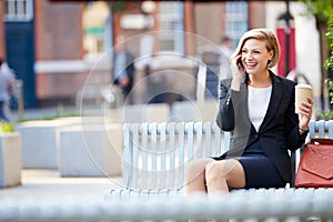 Businesswoman On Park Bench With Coffee Using Mobile Phone