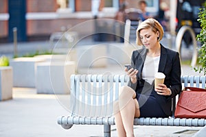 Businesswoman On Park Bench With Coffee Using Mobile Phone