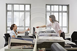 Businesswoman Passing Document To Colleague Over Desk In Office