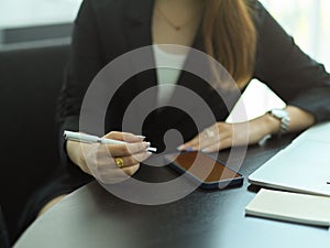 Businesswoman with pen in her hand working with smartphone and stationery
