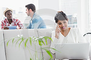 Businesswoman phoning and using laptop on couch