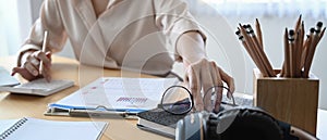 Businesswoman picking up her glasses and using calculator to calculate on office desk.