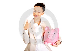 Businesswoman with piggybank and thumbs up.