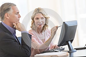 Businesswoman Pointing At Computer While Sitting With Colleague