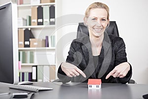 Businesswoman Pointing at Miniature House on Desk