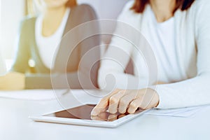 Businesswoman pointing at tablet computer screen while giving presentation to her female colleague. Group of business