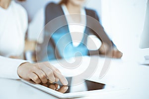 Businesswoman pointing at tablet computer screen while giving presentation to her female colleague. Group of business