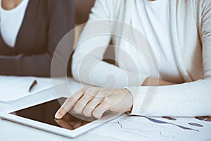 Businesswoman pointing at tablet computer screen while giving presentation to her female colleague. Group of business