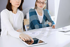 Businesswoman pointing at tablet computer screen while giving presentation to her female colleague. Group of business