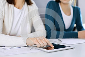 Businesswoman pointing at tablet computer screen while giving presentation to her female colleague. Group of business