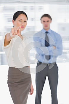 Businesswoman pointing towards camera with man in office