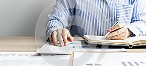 A businesswoman presses on a white calculator and looks at the numbers from a notebook she notes during a finance department