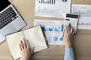 A businesswoman presses on a white calculator and looks at the numbers from a notebook she notes during a finance department