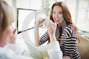 Businesswoman punching in air while discussing with colleague in creative office