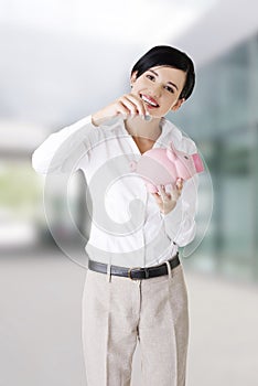 Businesswoman putting a coin into a piggy bank