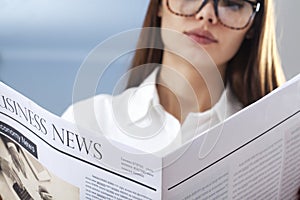 Businesswoman reading newspaper on gray background