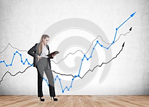 Businesswoman reading a notebook standing near rising stock market lines