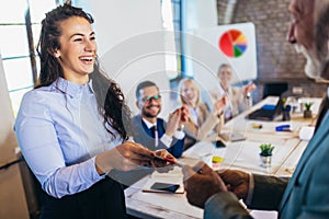 Businesswoman receiving award from businessman in front of business professionals, applauding at business seminar in office