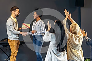 Businesswoman receiving award from businessman in front of business professionals, applauding at business seminar in office