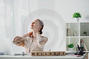 Businesswoman relaxing at workplace with laptop and alphabet cubes with wellness word