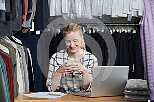 Businesswoman Running On Line Fashion Business In Warehouse Using Mobile Phone