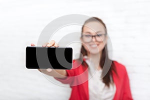 Businesswoman show cell smart phone screen with empty copy space wear red jacket glasses happy smile