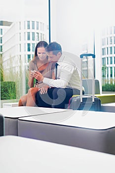 Businesswoman showing smartphone with businessman in hotel lobby